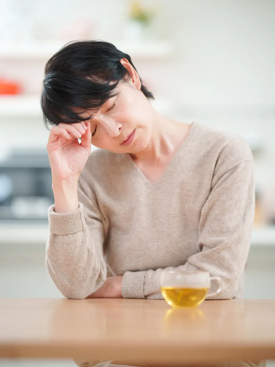 キッチンのテーブルで、こめかみに手をあてて目を閉じている女性
