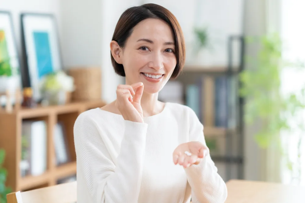 手のひらにのせたサプリメントを指でつまみ上げてほほえむ女性
